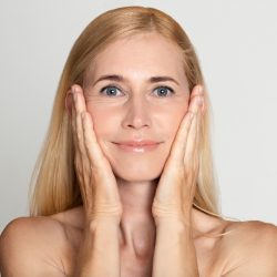 Anti aging treatment. Middle-aged woman touching cheeks over grey studio background